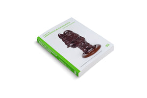 A book titled Lexikon der Lebensmittel als Kunstmaterial, shown at an angle on a white background. The white cover features a provocative, glossy brown sculpture of a garden gnome with a phallic shape and a flared base. The spine is bright green.