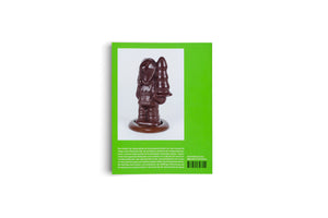 A studio shot of the back of a book with a bright lime-green cover against a white background. The cover features a photograph of a glossy, dark chocolate sculpture of a gnome-like figure holding a tall, conical object. Below the photograph is a block of German text, a barcode, and an ISBN.