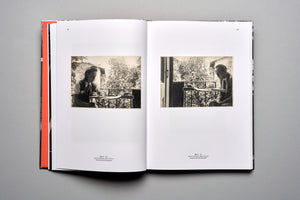 An open book on a gray surface, displaying a two-page spread with vintage black-and-white photographs. On the left page, a woman named Lola sits at a table on a balcony. On the right page, a man named Zwi sits at a similar table on a balcony. Both pages have captions in English.