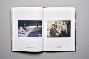 An overhead shot of an open book on a grey surface. The left page displays a color photograph from 1961 of a young boy and girl holding hands outside a modern building. The right page shows a black-and-white photograph from 1956 of the same two children standing by a bush in front of a brick building.