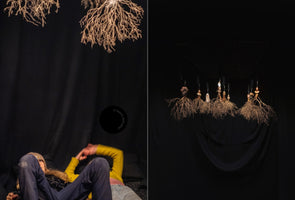 A diptych showing an art installation against a black background. On the left, a person lies down looking up at hanging, dried root sculptures. On the right, a closer view shows a row of the intricate root sculptures suspended from a grid on the ceiling.