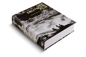 A thick, hardcover book titled Der Deutsche Film, shown at an angle against a white background. The cover features a dramatic black and white film still of a film crew with a camera on a vast, snowy mountain landscape. The title is printed in a bold, light yellow font on the cover and spine.