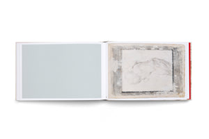 An overhead view of an open art book on a white background. The left page is a solid, pale sage green. The right page displays a charcoal drawing of an abstract, rounded form on aged paper, which is framed by a distressed, painted grey border.