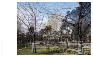 A composite photograph blending two different time periods in a park. A modern color scene with bare trees, green grass, and empty tables is overlaid with a ghostly, darker historical image. The older scene shows the same park filled with people and trees decorated with numerous round, white lanterns, creating a dreamlike effect where past and present coexist.