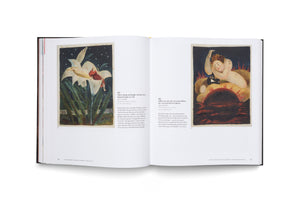 An open art book with a black spine lies on a white surface. The two-page spread displays colorful illustrations; the left shows a figure on a giant white lily against a starry sky, and the right shows a figure resting on a dark sun-like orb, both with accompanying German text.