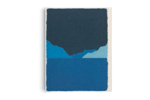 A vertical abstract artwork made of layered pieces of textured blue fabric on a white canvas. The composition suggests a landscape, with a dark navy blue shape like a sky or mountain range over smaller, lighter blue hills, all above a solid medium blue section resembling water.