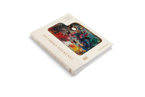 A hardcover book with a cream-colored fabric cover, set against a white background. The front cover features the German title DIE FARBEN DER KUNST in gold lettering and an image of a wooden artist's palette covered in a thick, vibrant mix of many colors of paint. The book is angled to show the cover and the spine.