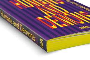 A close-up, angled view of a book with a vibrant purple-striped cover. The title, Humans and Demons, is in large, blocky letters with a red and yellow striped pattern. The book has bright yellow page edges and is set against a white background.