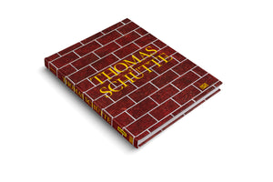 A hardcover book titled Thomas Schütte lies at an angle on a white surface. The cover is designed to look like a red brick wall with white mortar lines, and the title is printed in a large, yellow serif font. The spine is also visible.