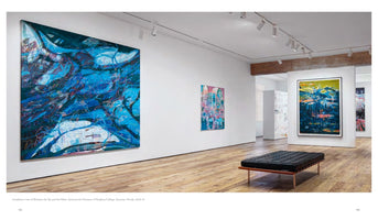 An installation view of an art exhibition in a modern gallery with white walls and light wood floors. On the left, a very large, dynamic abstract painting in shades of blue hangs on the wall. A black tufted leather bench sits in the center of the room, and other colorful abstract paintings are visible in the background.