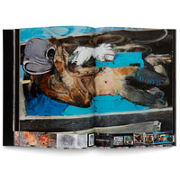 An open art book photographed against a white background, displaying a two-page spread of an abstract expressionist painting. The painting shows a distorted, reclining figure with a grey head on a vibrant blue and black background. Below the main image, there is a row of smaller thumbnail images showing sketches and related artworks.