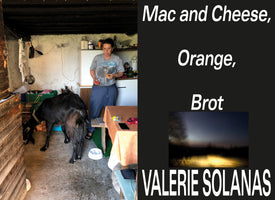 A collage-style image. On the left, a photo shows a woman in a rustic kitchen standing near a large black goat that is eating from a bowl. On the right is a black background with white text that reads Mac and Cheese, Orange, Brot, and VALERIE SOLANAS, with a small, blurry photo of a dark landscape in between.
