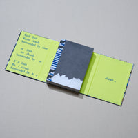 An open art book lies on a neutral surface. The book has a patterned exterior and bright lime-green inner covers. The left inner cover has fragmented blue text, and the right inner cover reads alia ali... The book block has a dark gray cover that is torn at the bottom, revealing white, textured pages underneath, and a decorative blue and white headband at the spine.