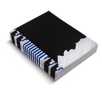 An angled shot of a thick book with a modern, graphic design, set against a white background. The cover is matte black with a jagged, torn edge on the right, revealing a textured white and grey abstract pattern underneath. The spine has a bold geometric design of black blocks alternating with sections of blue and white diagonal stripes.