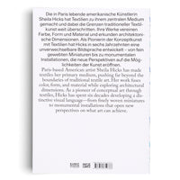 A close-up of a white book cover with black text. The text, in German and English, describes Paris-based American artist Sheila Hicks and her pioneering work in textile art. At the bottom are the logos of Kunst Museum St. Gallen and Hatje Cantz, along with an ISBN and a barcode.