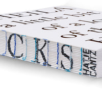 A close-up, angled view of a book's spine with an exposed Coptic stitch binding. The thick stack of white pages is sewn together with bright blue and aqua thread. Large, black letters are printed on the fore-edge of the pages, creating a textual pattern along the spine.