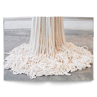 A photograph in an open book shows a contemporary art installation made of thick, off-white rope. A dense curtain of ropes hangs vertically from an unseen point, pooling into a large, tangled mass on the grey concrete floor below.