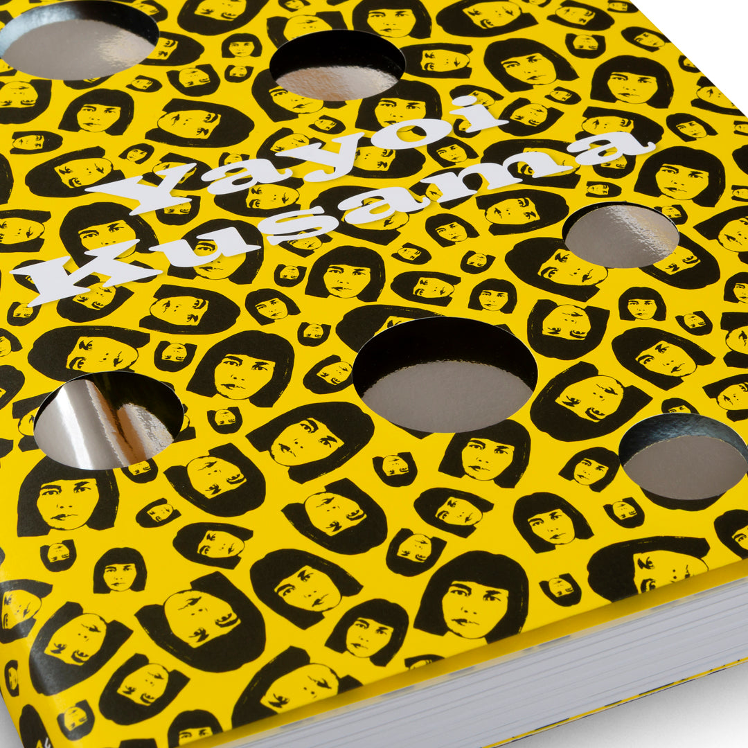 A close-up of a book cover with a bright yellow background and a repeating pattern of a black stylized portrait of artist Yayoi Kusama. The cover has several circular holes cut out, revealing a reflective silver material underneath. Her name is printed across the top in white, wavy letters.