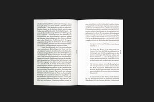 An overhead shot of an open book with German text laid flat on a dark surface. The text is set in a two-column layout on white pages, with the page markers DE 027 and DE 028 printed vertically in the outer margins.