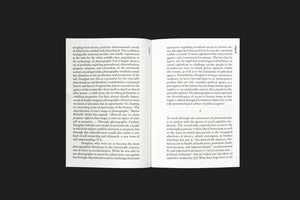 A top-down photograph of an open book, displaying two pages of dense black text on white paper. The book is set against a solid, dark background, creating a stark contrast.