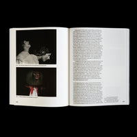 An overhead view of an open book on a dark surface, showing pages 108 and 109. The left page features two photographs of artist Meredith Monk's work, while the right page is filled with printed text about her career.