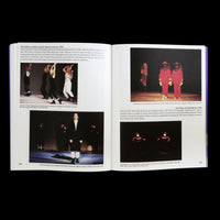 An open book displays a two-page spread, pages 338 and 339, about the 1996 performance The Politics of Quiet. The pages feature text and four color photographs showing performers on stage in various scenes and costumes, including dancers in motion and two figures in bulky red hooded suits.