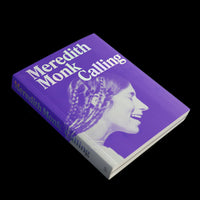 A hardcover book titled Meredith Monk Calling, set against a black background. The book has a vibrant purple cover with a profile photograph of a smiling woman with braided hair, tinted in purple and white. The title is printed in a bold, white serif font.