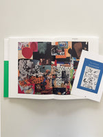 An overhead shot of an open book lying on a white surface. The book's pages display a dense, colorful collage of various images, including a classical sculpture, an x-ray, and abstract patterns. A smaller, separate booklet with a blue cover titled Steve Dickison, DISPOSED lies on the right-hand page.