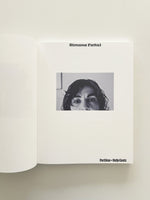 An open book on a white surface. The right page shows the title Simone Fattal at the top, a central black-and-white cropped photograph of a woman's face showing her eyes and dark hair, and the text Portikus + Hatje Cantz at the bottom.