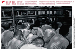 A stark black and white photo on a magazine page shows a large group of male prisoners with shaved heads packed tightly together in a prison in El Salvador. One man in the center turns to look directly at the camera, his face standing out from the crowded, somber scene.