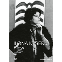 A black and white photograph of artist Ilona Keserü in a fuzzy coat, standing thoughtfully in front of an abstract painting with wavy stripes.