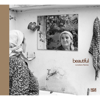 A black and white photograph of an older woman in a headscarf, seen from behind as she looks at her reflection in a mirror hanging on an outdoor wall.