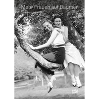 A vintage black and white photograph of two smiling women sitting together on a tree branch.