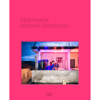 The pink cover of the book Matrimania by Mahesh Shantaram, featuring a photo of a woman in a blue sari dancing on a rooftop decorated with string lights at dusk.