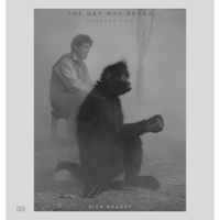A black-and-white photograph shows a spider monkey in the foreground and a man sitting on a stool in the hazy background.