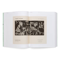 An angled, overhead photograph of an open book with a light green spine against a white background. The book displays a two-page spread featuring a black-and-white reproduction of Pablo Picasso's painting Guernica, with text in both Roman and Arabic scripts.