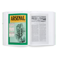 An angled photograph of an open book on a white surface. The left page is a vibrant green and features the title Arsenal Surrealist Subversion in a yellow box above a surreal black-and-white illustration. The right page displays two columns of text below a black-and-white photograph of an icy landscape.