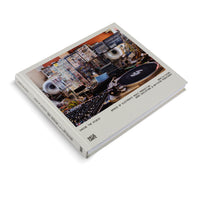A hardcover book titled Inside the Studio shown at an angle on a white background. The front cover features a photograph of a dense electronic music studio, filled with a modular synthesizer, a tangle of colorful wires, a mixing console, and a turntable. The title is printed in a simple sans-serif font on the off-white cover.