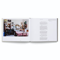 An overhead shot of an open book on a white surface. The left page shows a color photograph of a cluttered artist's studio and kitchen. The right page features the text of an interview with Giulia Valenti.