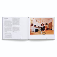 An open book showing a two-page spread. The left page features text from an interview with Sarah Farina. The right page is a full-color photograph of Farina, a woman with dark curly hair, sitting in a modern black chair at a white desk in a sunlit room. A guitar hangs on the wall behind her, and music equipment is on the desk.