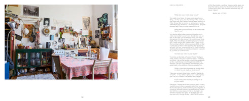 A two-page magazine spread featuring an interview with Giulia Valenti. The left page is a full-bleed photo of her cluttered, eclectic home studio, which doubles as a kitchen and dining area. A table with a pink floral tablecloth is in the foreground, with a kitchen counter, stove, and a green cabinet in the background. The walls are covered with posters, photos, and hanging pots. The right page contains the text of the interview.