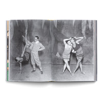 An open book displays a two-page, black-and-white photograph of four dancers in a studio. On the left, a man in a striped top and knickerbockers holds the leg of a woman performing a one-handed handstand. On the right, two women in short, striped outfits pose closely together in front of a painted, abstract backdrop.