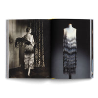 An open book with a two-page spread on a 1920s flapper dress. The left page shows a vintage black-and-white photo of a woman modeling the beaded fringe dress with a large feather fan. The right page shows a modern color photo of the same dress on a mannequin against a black background.