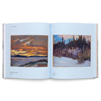 An open art book displaying two landscape paintings by J.E.H. MacDonald on light blue pages. The painting on the left depicts a vibrant, cloudy sunset over a lake, while the painting on the right shows a snowy landscape in front of a dense forest.