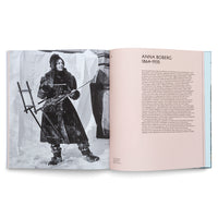 An open art book showing a two-page spread. The left page has a full-page, black-and-white photo of artist Anna Boberg in heavy winter clothing, standing in the snow and holding a portable easel and painting equipment. The right page features her name, dates 1864-1935, and a biography in German.