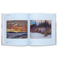 A photograph of an open art book showing a two-page spread of paintings by J.E.H. MacDonald. The left page features an impressionistic painting of a fiery orange sunset over a lake. The right page shows a winter landscape with a snow-covered foreground and a dark forest in the background.
