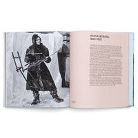 An open book with a two-page spread. The left page features a full-page, black-and-white photograph of artist Anna Boberg dressed in heavy winter gear, standing in the snow and holding a portable easel. The right page is a biography of the artist, headed with the title ANNA BOBERG 1864-1935.