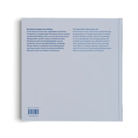 The back cover of a pale blue hardcover book, shown at an angle on a white background. The cover features two columns of text, one in German and one in English, describing the work of photographer Frank Kunert under the titles Die Widersinnigkeit des Alltags and The Absurdity of Everyday Life. An ISBN, barcode, and the publisher's name, Hatje Cantz, are visible at the bottom.
