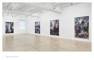 A wide-angle interior view of a modern art gallery with white walls and a polished concrete floor. Four large, vertical abstract paintings are spaced out along the walls. The artworks feature dark, smudged backgrounds covered with energetic, colorful scribbles and gestural lines in red, blue, and orange.