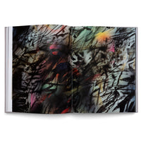 An open book lies flat on a white background, displaying a two-page spread of abstract, graffiti-style art. The piece features a dense and chaotic composition of black spray-painted lines and stenciled shapes layered over a colorful background with gradients of pink, orange, yellow, and green.